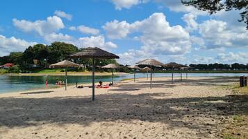 Una playa con sombrillas, un lago y cielo despejado.