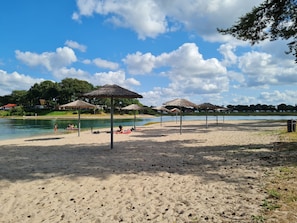 A beach with umbrellas, a lake, and a clear sky.