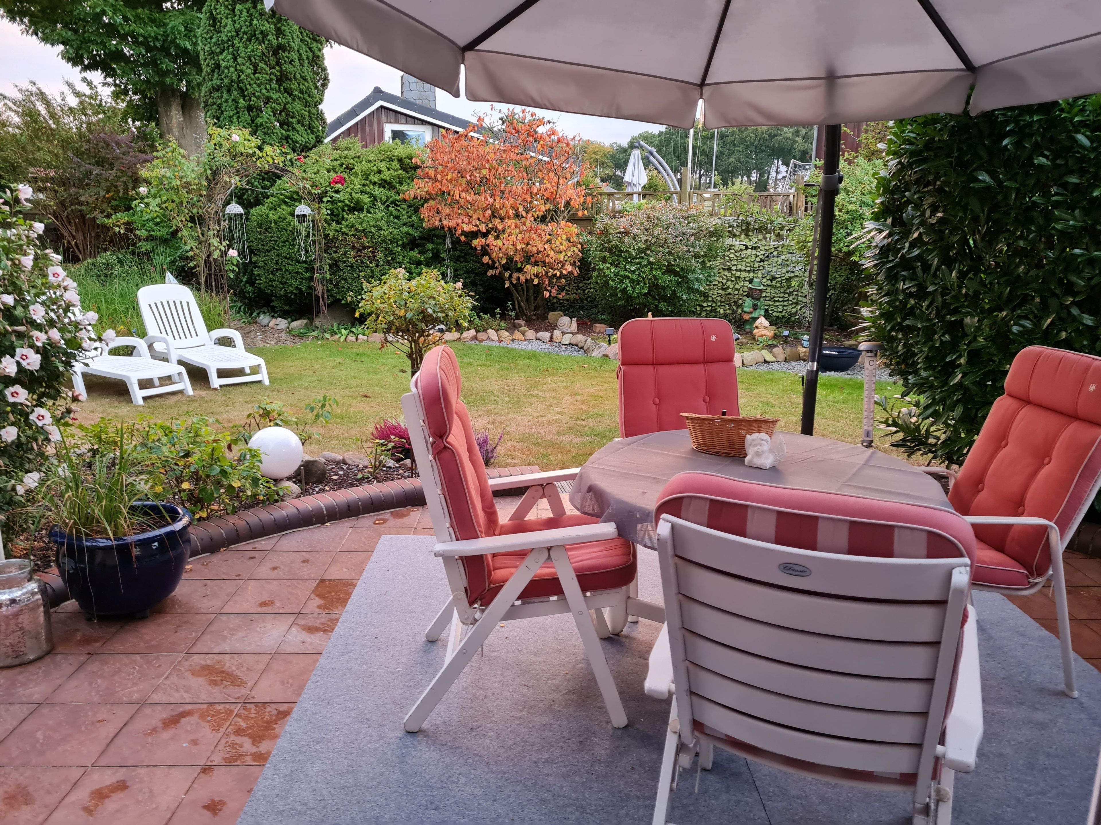 An outdoor patio with a round table, red and white chairs, and a large umbrella.