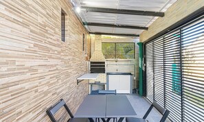 A compact outdoor dining area with a brick wall, a metal-framed table, and a green shutter door. - Inn in Condo. w/ BBQ nr. Beto CW Pms0010 (Penha)