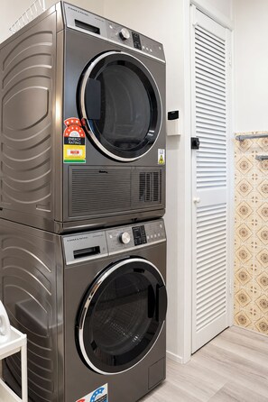 A stacked washer and dryer unit with a control panel, energy rating sticker, and a warning label. - Cozy Bentleigh Family Retreat (Bentleigh)