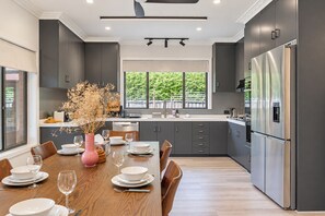 A modern kitchen with grey cabinets, a stainless steel refrigerator, and a dining area with a wooden table set for four. - Cozy Bentleigh Family Retreat (Bentleigh)