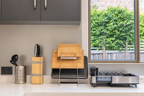 A kitchen with a window view, a knife block, a colander, and a wooden cutting board. - Cozy Bentleigh Family Retreat (Bentleigh)