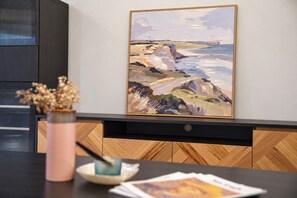 A room with a wooden herringbone floor, a black cabinet, a framed painting on the wall, a pink vase with dried flowers, and a small white bowl on a table. - Cozy Bentleigh Family Retreat (Bentleigh)