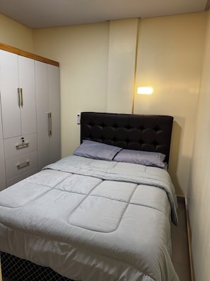 Et soveværelse med seng, garderobe og vægmonteret lampe.