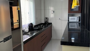 A modern kitchen with a refrigerator, stove, microwave, and yellow pendant lights. - EAM COMPLEXO RESIDECIAL Apto 07 (Bela Vista de Goiás)