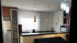 A modern kitchen with a black sofa, a refrigerator, a microwave, and pendant lights. - EAM COMPLEXO RESIDECIAL Apto 07 (Bela Vista de Goiás)