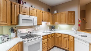 A kitchen with wooden cabinets, a microwave, stove, sink, and a coffee maker. - Smugglers Notch | Snowy Retreat | Ski, Pools & Mountain Fun (Jeffersonville)