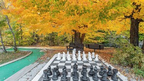 A large outdoor chessboard set up in a park with trees in autumn colors. - Smugglers Notch | Ski Escape | Pool & Slopes | 2BR Suite (Jeffersonville)