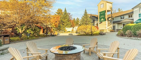 Une cour avec des fauteuils Adirondack, un foyer en pierre et un bâtiment doté d’une tour horlogée et d’une enseigne.