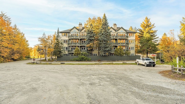 A multi-story building with balconies, surrounded by trees with autumn foliage.