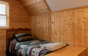 Ein Zimmer in einer Holzhütte mit einem Bett, einem Fenster und einer Holzbank.