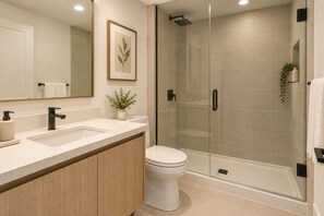 Un baño moderno con ducha envuelta en vidrio, inodoro blanco y tocador con lavamanos y una planta.