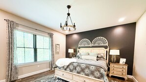 A bedroom with a large bed, a nightstand, a chandelier, and a window with curtains. - Modern Farmhouse In Salem (Salem)
