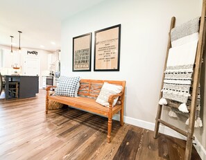 A wooden bench with cushions, a woven wall hanging, and two framed signs on the wall.