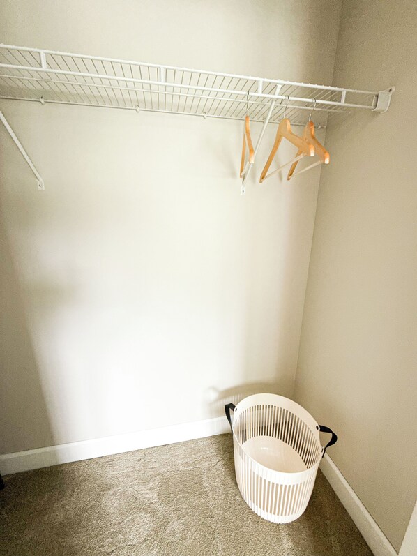 A corner of a room with a white laundry basket and a white metal drying rack with wooden hangers.