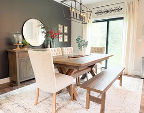 A dining area with a wooden table, cushioned chairs, a bench, a chandelier, and a large mirror. - Modern Farmhouse In Salem (Salem)