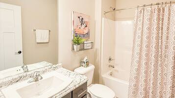 A bathroom with a double sink vanity, toilet, bathtub, and shower curtain.