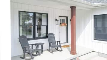Eine Veranda mit zwei Schaukelstühlen, einem kleinen Tisch und einer Tür mit einem Kranz.