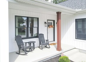 A porch with two rocking chairs, a small table, and a door with a wreath.