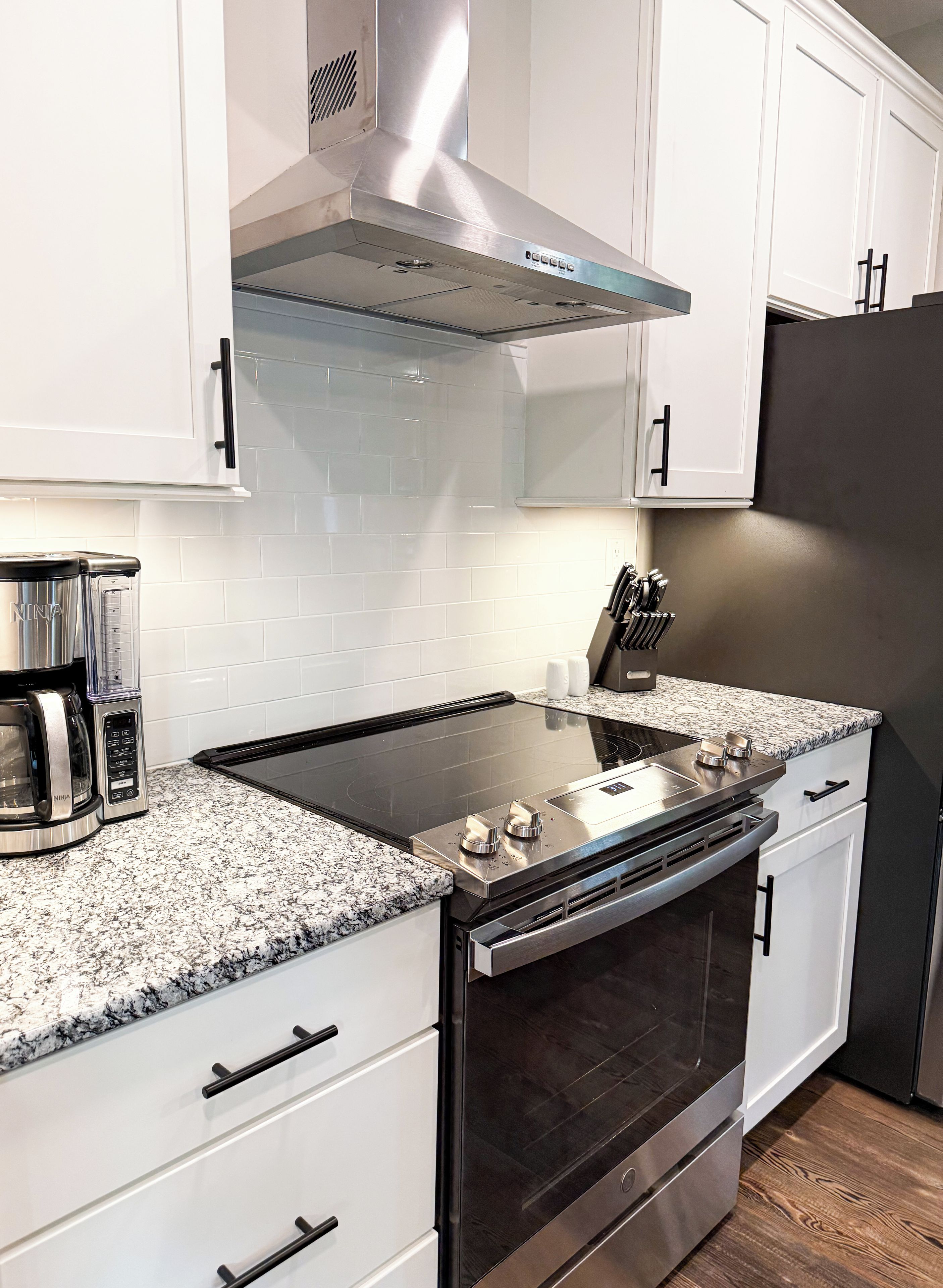 A kitchen with white cabinets, a stainless steel range hood, a black stovetop, and a built-in oven.