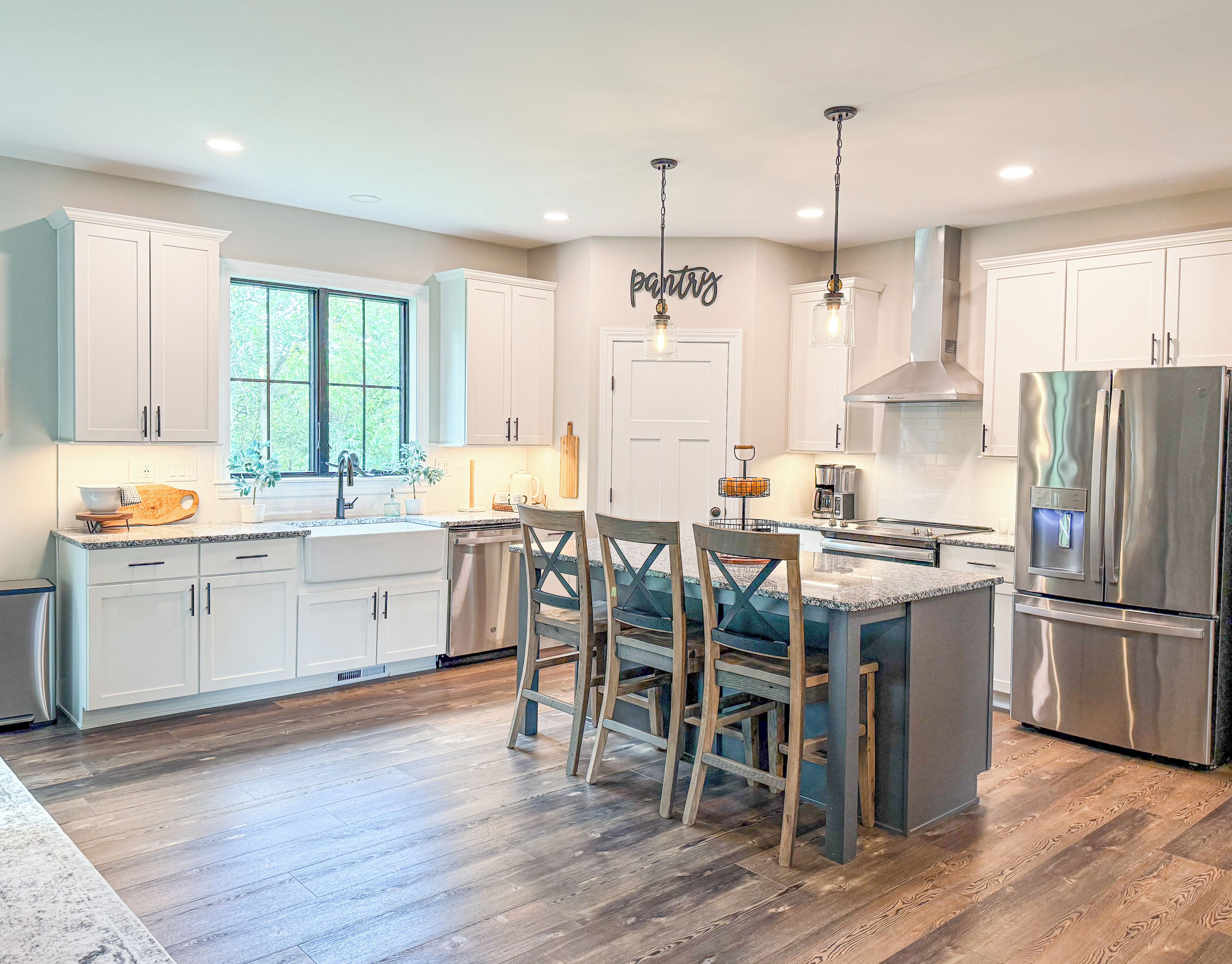 A modern kitchen with white cabinets, a stainless steel refrigerator, and a large window.