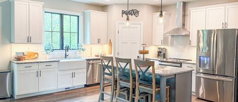 A modern kitchen with white cabinets, a stainless steel refrigerator, and a large window.