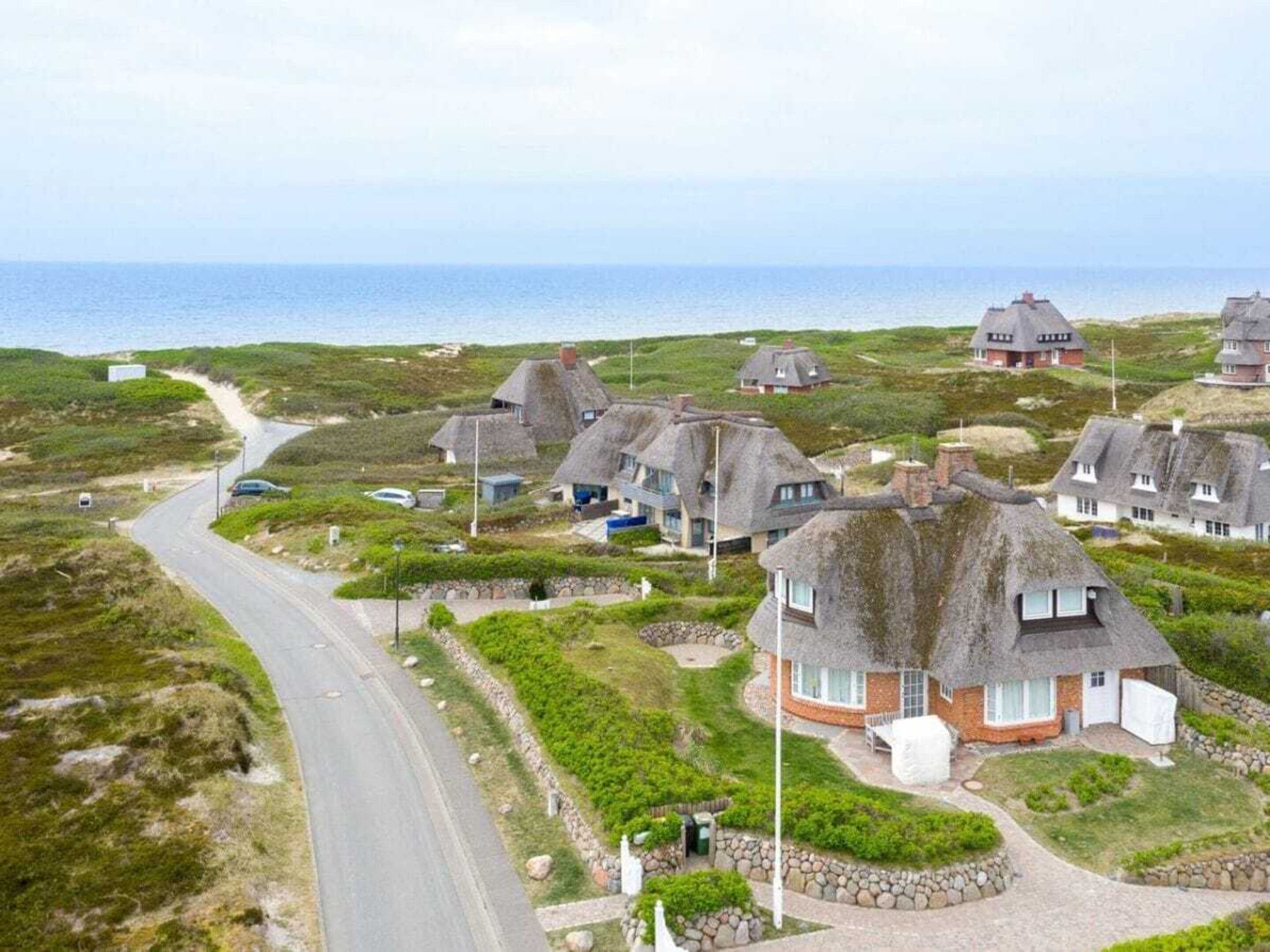 A coastal village with thatched-roof houses, a winding road, and a view of the sea.
