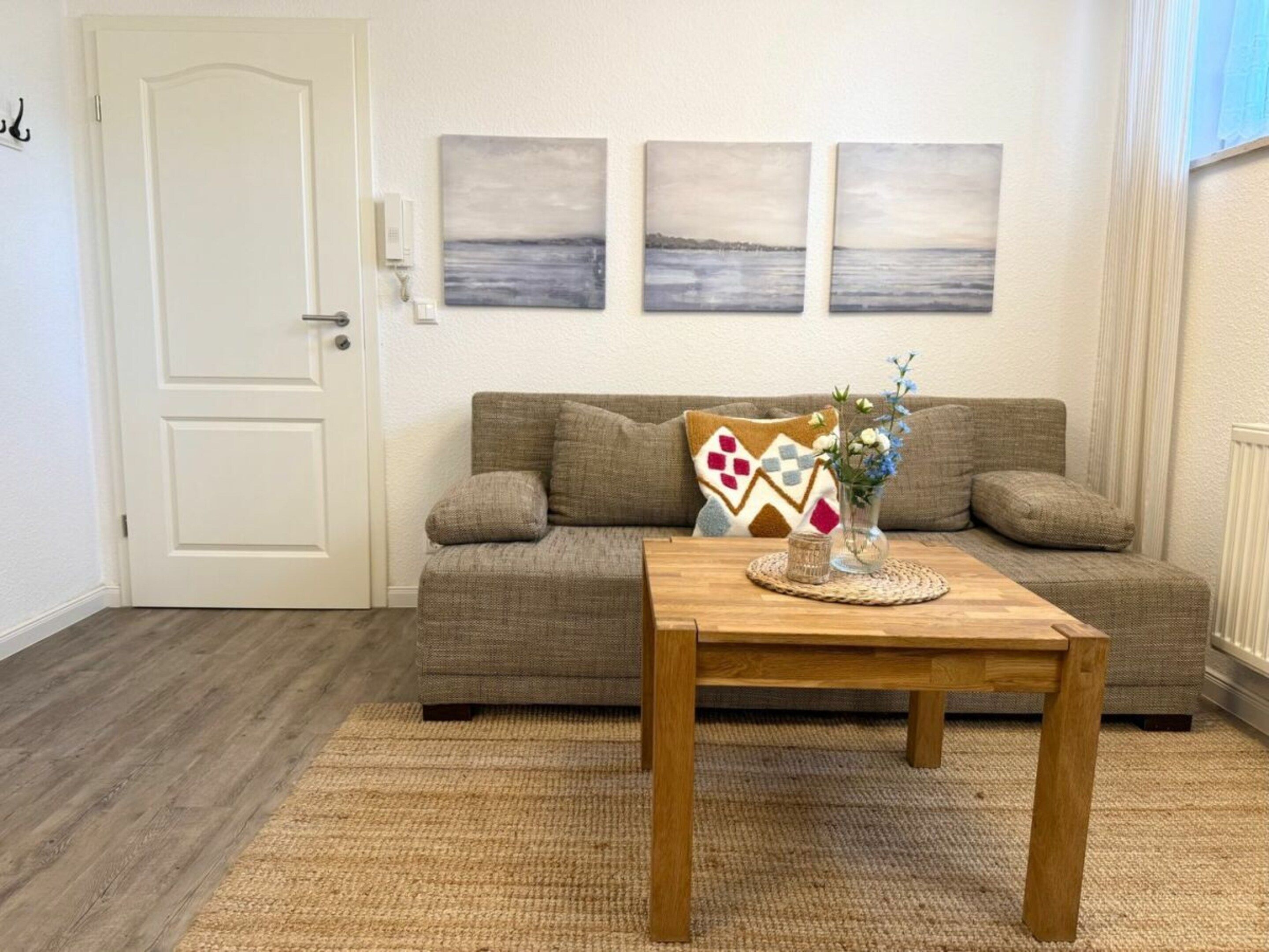 Ein Wohnzimmer mit einer Couch, einem Holztisch mit einer Vase und zwei an der Wand hängenden Bildern.