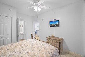 Ein Schlafzimmer mit einem Bett, einem Schminktisch, einem an der Wand befestigten Fernseher und einem Deckenventilator.