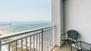 Varanda com vista para a praia e oceano, uma cadeira de metal e um corrimão branco.