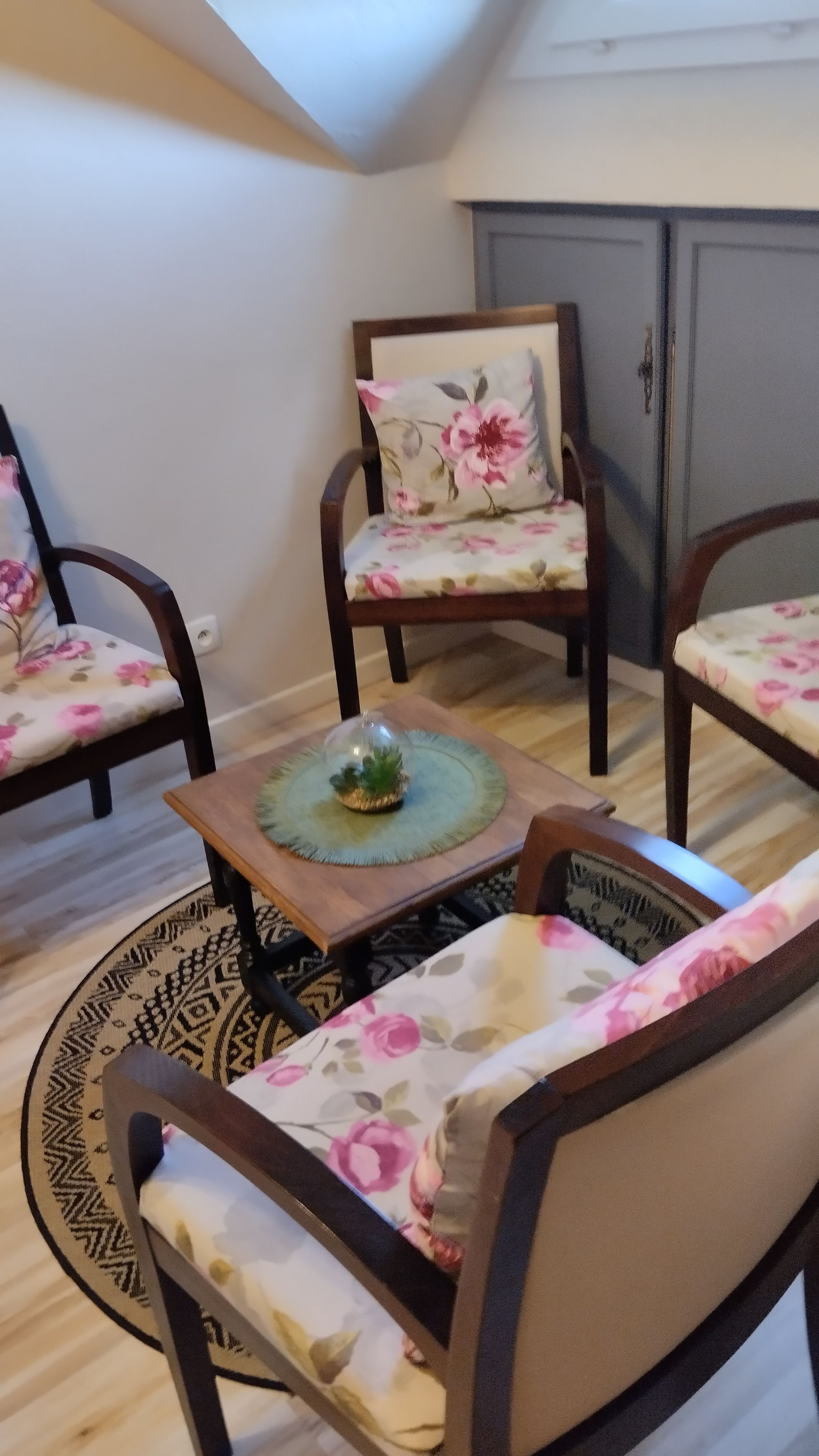 A room with a high ceiling, wooden flooring, and floral-patterned furniture including chairs and a sofa.