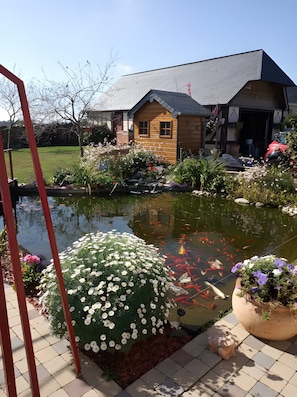Un estanque con peces koi, rodeado por una casa de madera y un jardín con flores.