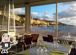 En restaurang med bord dukade för middag, utsikt över havet och en tecknad figur.
