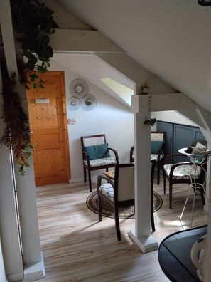 Une pièce avec une porte en bois, deux chaises dotées de coussins à motifs, une petite table ronde et un élément décoratif mural.