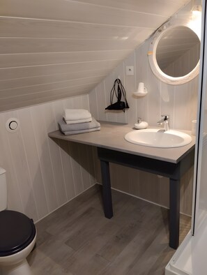 Un baño con tocador blanco, espejo redondo, toallero y retrete.