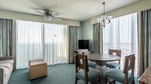 A hotel room with a ceiling fan, a television, a round dining table with chairs, and a large window with curtains. - North Myrtle Beach | Seaside Escape | Pool & Beach (North Myrtle Beach)