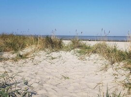 A sandy beach with grass in the foreground and a clear sky.