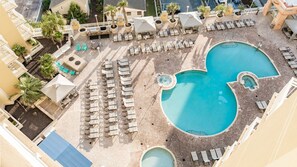 Eine Luftaufnahme eines Resorts mit mehreren Schwimmbecken, Liegestühlen und Palmen.