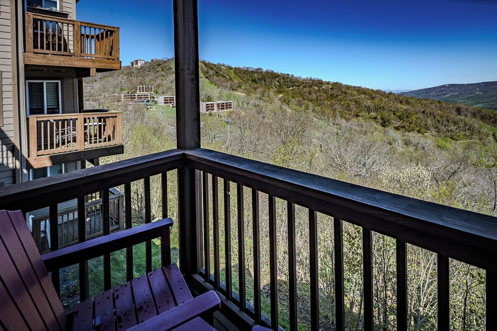 A balcony with a view of a hilly landscape, wooden railings, and a bench.