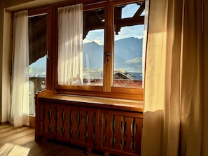 Ein Zimmer mit einem Holsterfenster und Blick auf Berge, inklusive einer Holzbank.