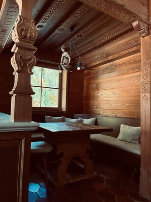 Un interior de madera con una zona de asientos con banco, una mesa y una lámpara colgante.