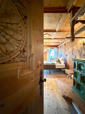 Ein Holzinnenraum mit einer geschnitzten Tür, einem Bett mit Kissen und einem grünen Schrank.