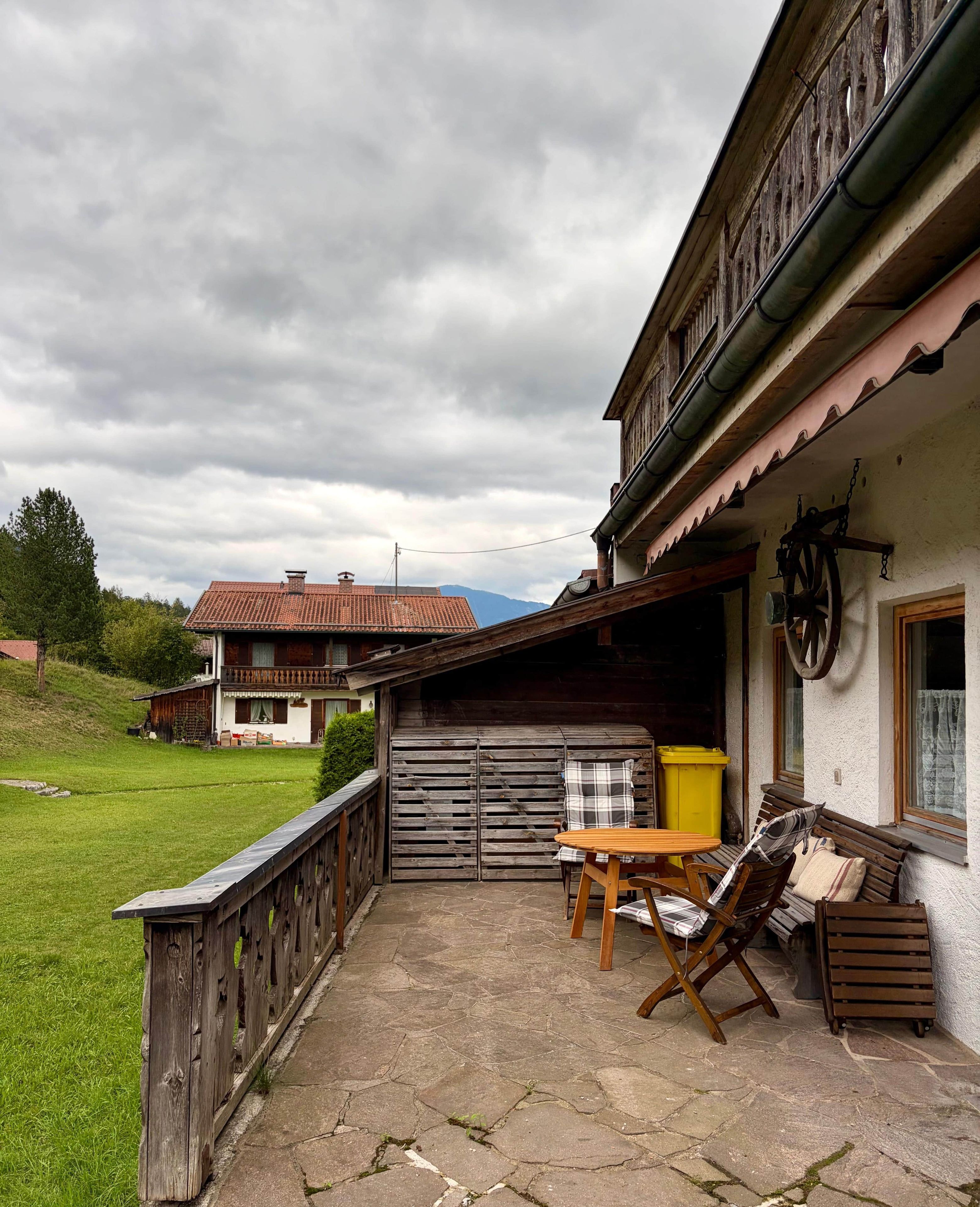 Eine rustikale Außenveranda mit Holztisch und -stühlen, einem Holzzaun und einem Gebäude mit geneigtem Dach.