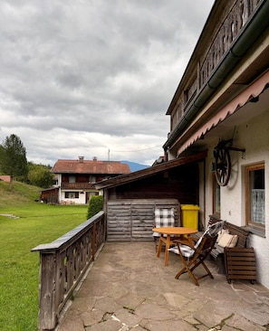 Eine rustikale Außenveranda mit Holztisch und -stühlen, einem Holzzaun und einem Gebäude mit geneigtem Dach.