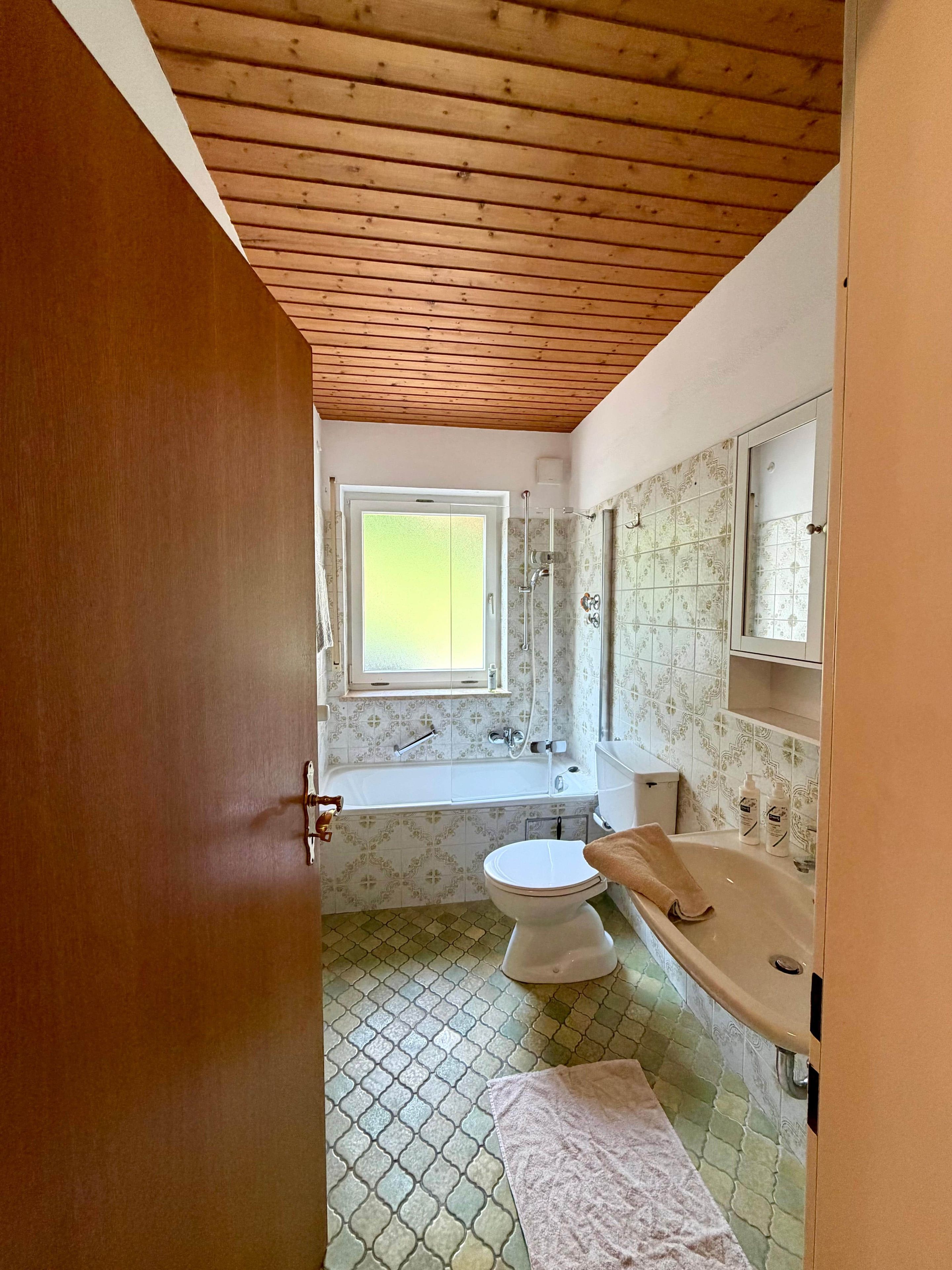 Ein Badezimmer mit Holzboden, einem Fenster, einer Badewanne, einer Toilette und einem Waschbecken.