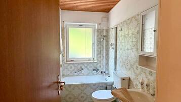Ein Badezimmer mit Holzboden, einem Fenster, einer Badewanne, einer Toilette und einem Waschbecken.