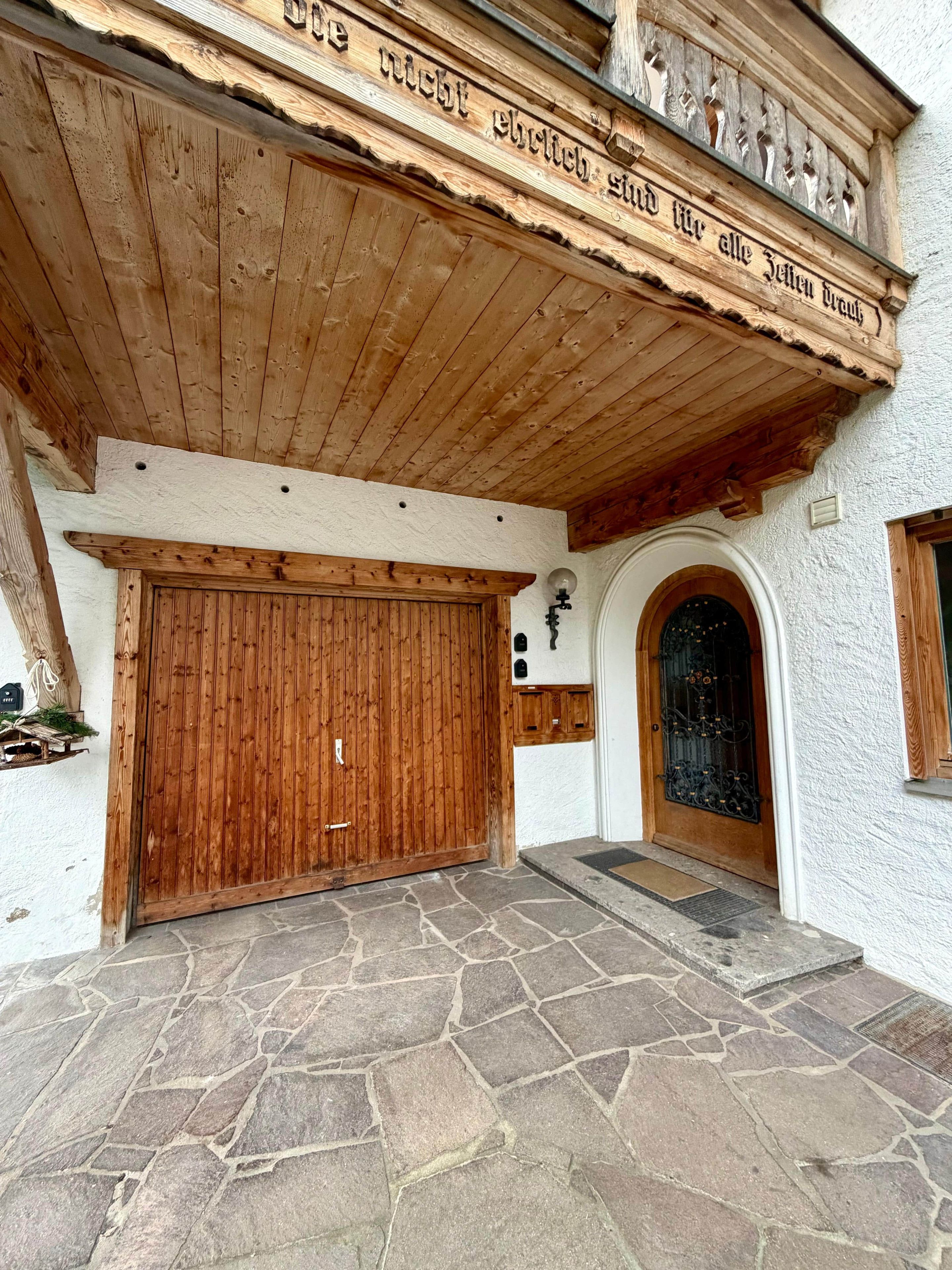 Ein Gebäude mit einer Holzfassade, einem gepflasterten Eingangsbereich und einer großen Holztür.
