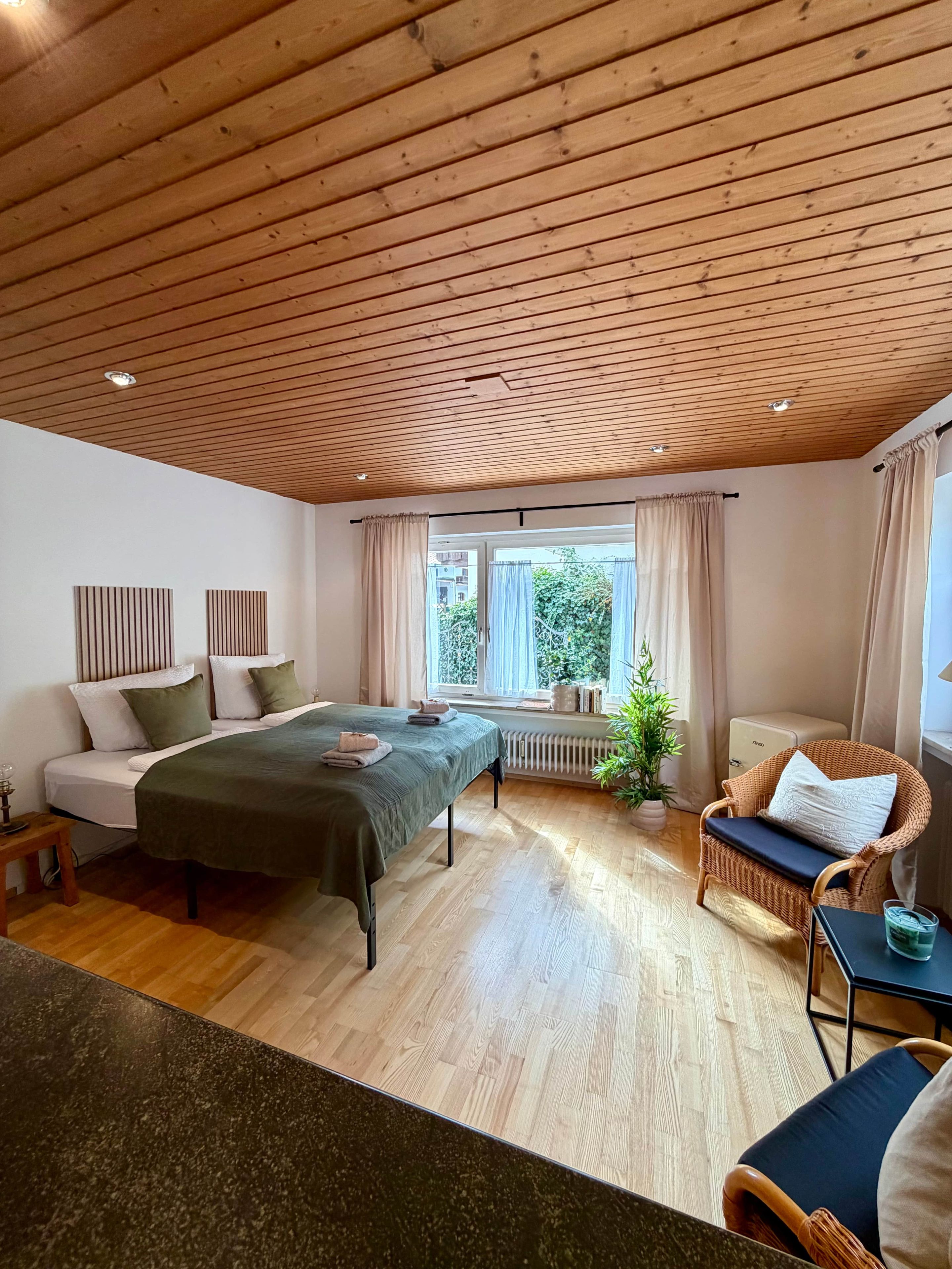 Una habitación con cama, sofá, sillón de mimbre y radiador.