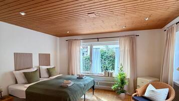 Una habitación con cama, sofá, sillón de mimbre y radiador.